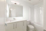 This modern bathroom features a sleek vanity with a white countertop and ample storage, complemented by a large mirror and a stylish vanity light.
