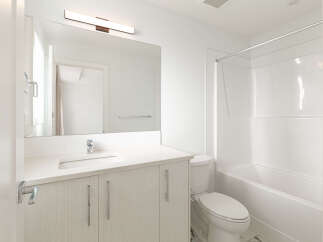 This modern bathroom features a sleek vanity with a white countertop and ample storage, complemented by a large mirror and a stylish vanity light.