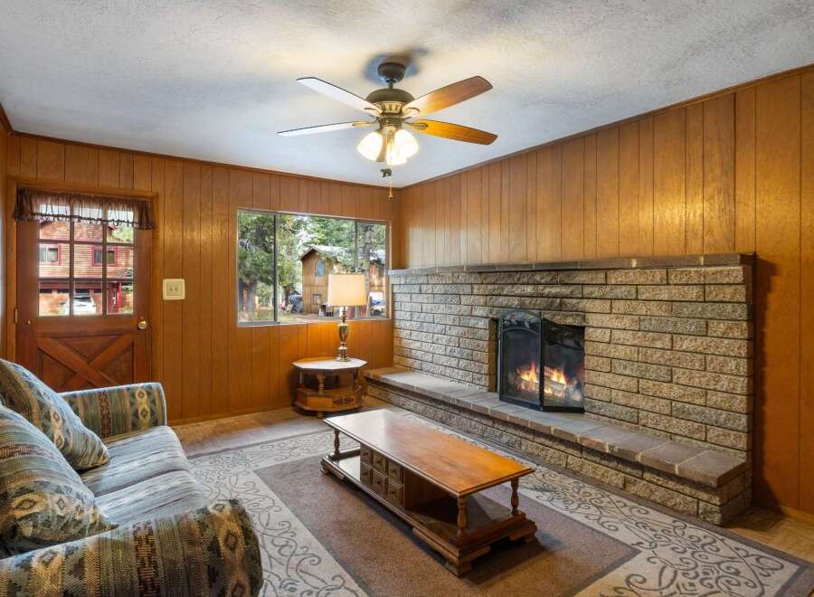 Cozy up by the stone fireplace in this inviting living room, featuring warm wood paneling and a comfortable sofa.