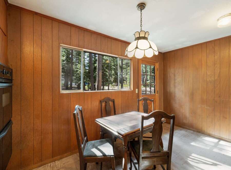 Enjoy a cozy dining experience in this charming room featuring warm wood-paneled walls and a large window overlooking a serene forest.
