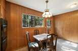 Enjoy a cozy dining experience in this charming room featuring warm wood-paneled walls and a large window overlooking a serene forest.