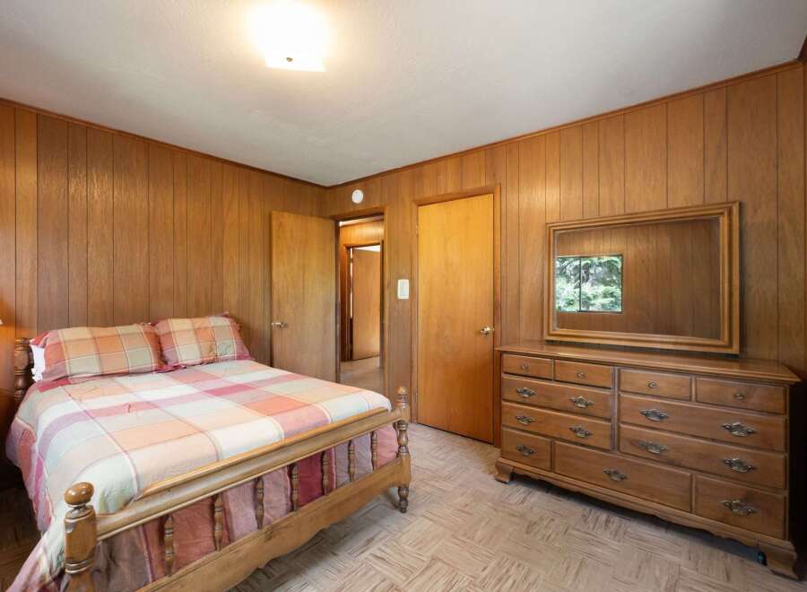 Step into a cozy bedroom featuring warm wood-paneled walls and a comfortable bed with a plaid comforter.