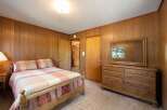Step into a cozy bedroom featuring warm wood-paneled walls and a comfortable bed with a plaid comforter.