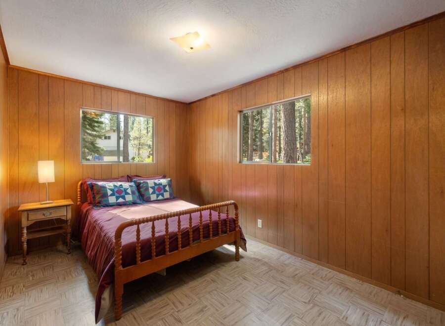 Experience cozy living in this charming bedroom featuring warm wood-paneled walls and a comfortable bed adorned with decorative pillows.