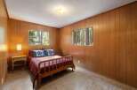Experience cozy living in this charming bedroom featuring warm wood-paneled walls and a comfortable bed adorned with decorative pillows.