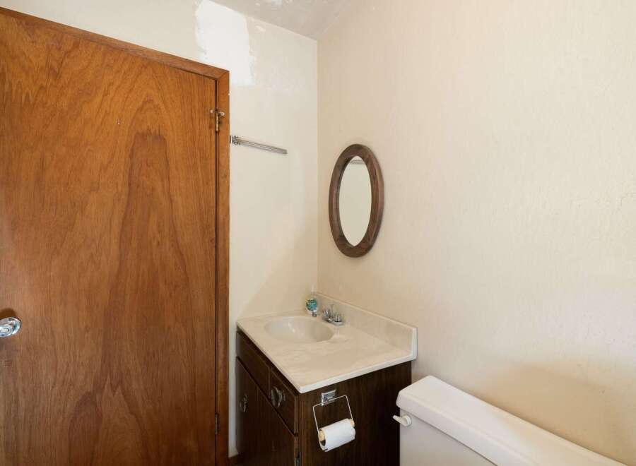 This bathroom features a classic wooden door, a vanity with a sink and mirror, and a toilet.