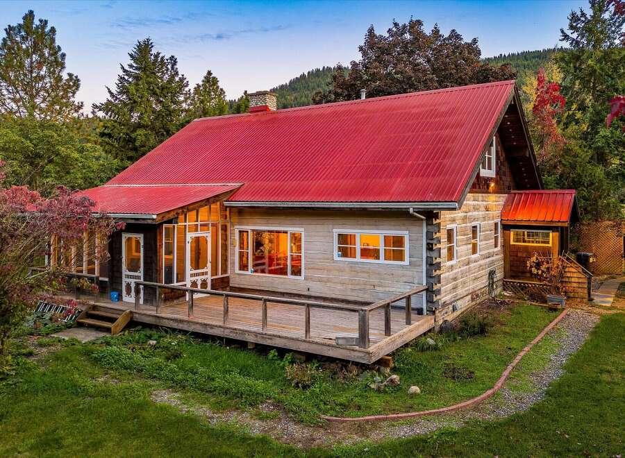 Experience rustic charm in this log cabin featuring a vibrant red metal roof and expansive wooden deck, perfect for enjoying the surrounding natural beauty.