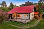 Experience rustic charm in this log cabin featuring a vibrant red metal roof and expansive wooden deck, perfect for enjoying the surrounding natural beauty.