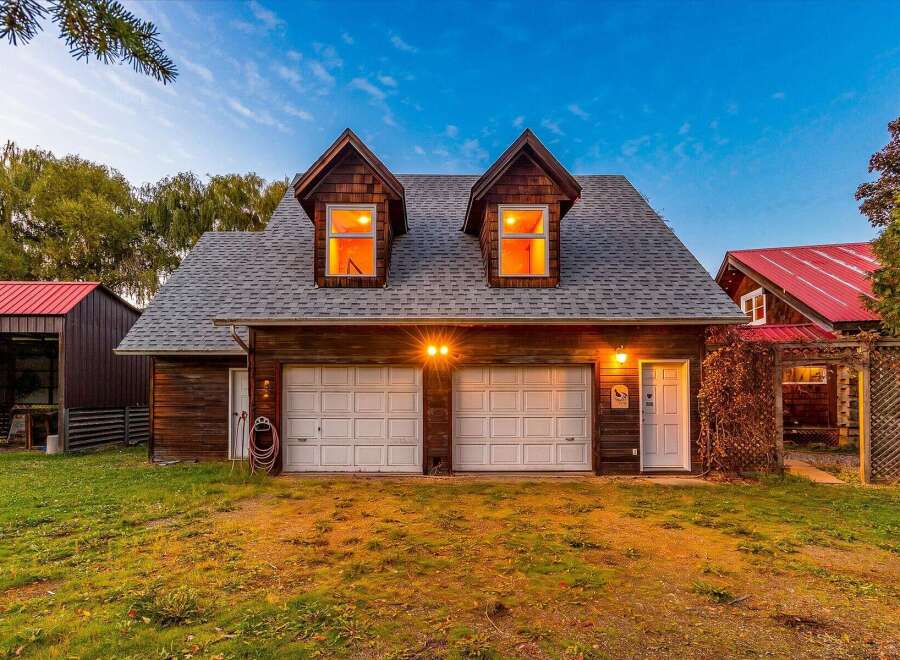 This charming property features a rustic wooden exterior with a classic gambrel roof, complemented by two dormer windows that cast a warm glow.