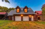 This charming property features a rustic wooden exterior with a classic gambrel roof, complemented by two dormer windows that cast a warm glow.