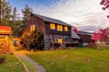 Experience rustic charm with this multi-story wooden home, featuring warm, illuminated windows that suggest a cozy interior.