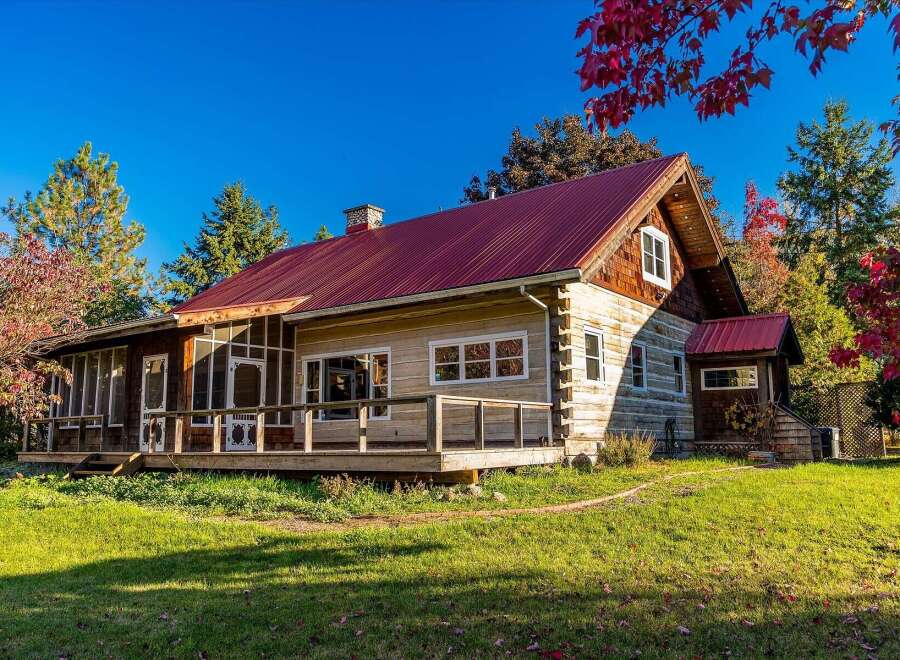 Experience rustic charm in this beautiful log cabin featuring a vibrant red metal roof and a spacious wrap-around porch perfect for enjoying the crisp autumn air.