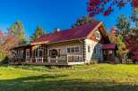 Experience rustic charm in this beautiful log cabin featuring a vibrant red metal roof and a spacious wrap-around porch perfect for enjoying the crisp autumn air.