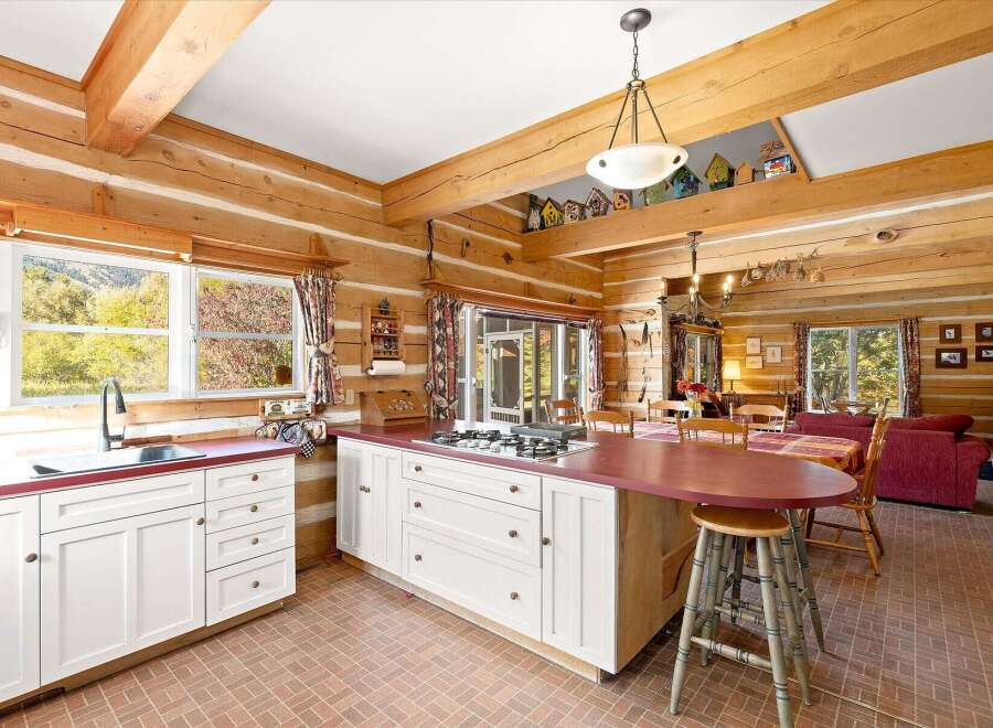 Experience rustic charm in this log cabin kitchen, featuring white cabinetry, a gas stovetop, and a large island with a burgundy countertop.