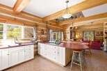 Experience rustic charm in this log cabin kitchen, featuring white cabinetry, a gas stovetop, and a large island with a burgundy countertop.