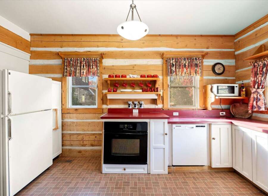 Step into this charming log cabin kitchen, featuring rustic wood paneling and cozy red countertops.