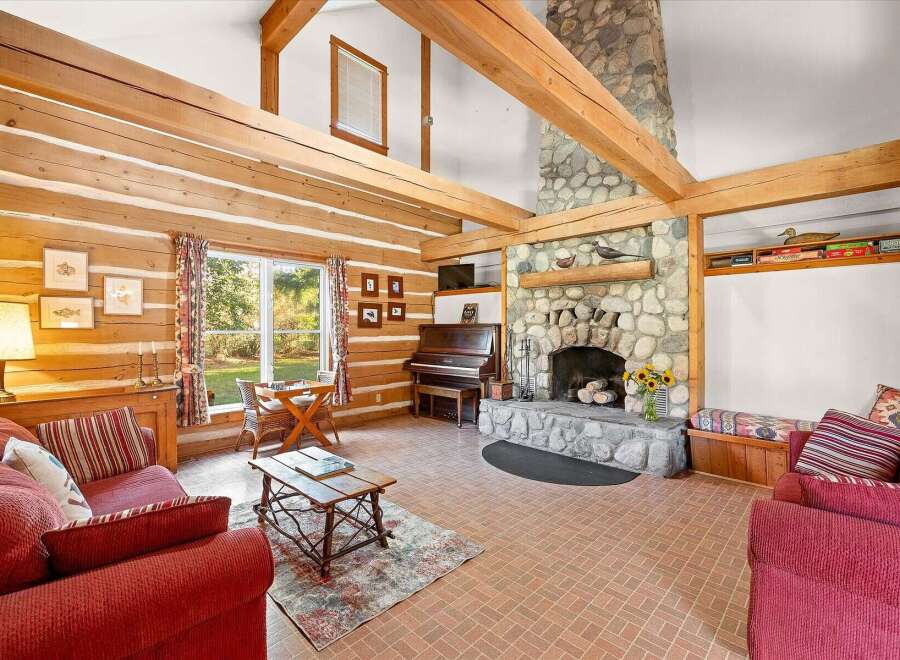 Experience rustic charm in this inviting log cabin living room, featuring a grand stone fireplace and exposed wooden beams that create a warm, cozy atmosphere.