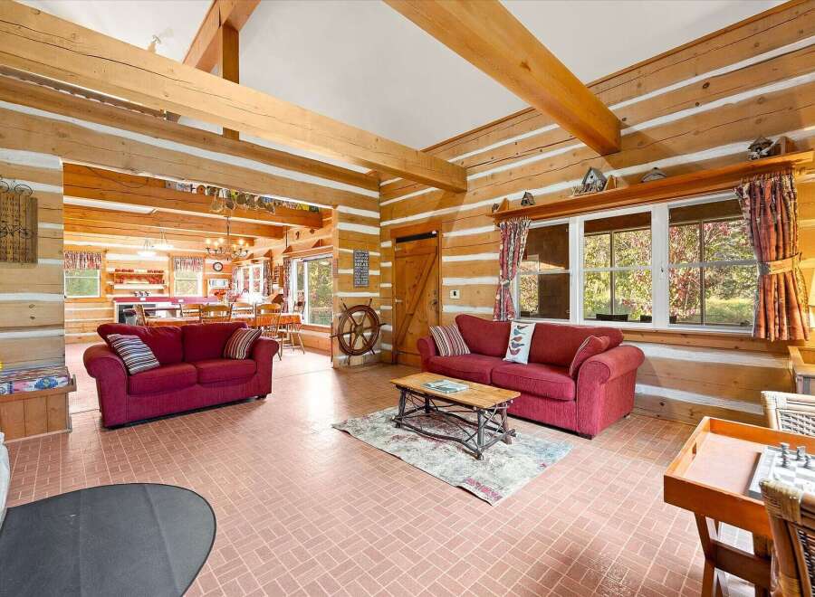 Step into this charming log cabin living room, featuring a cozy seating area with two plush red sofas and a rustic coffee table.