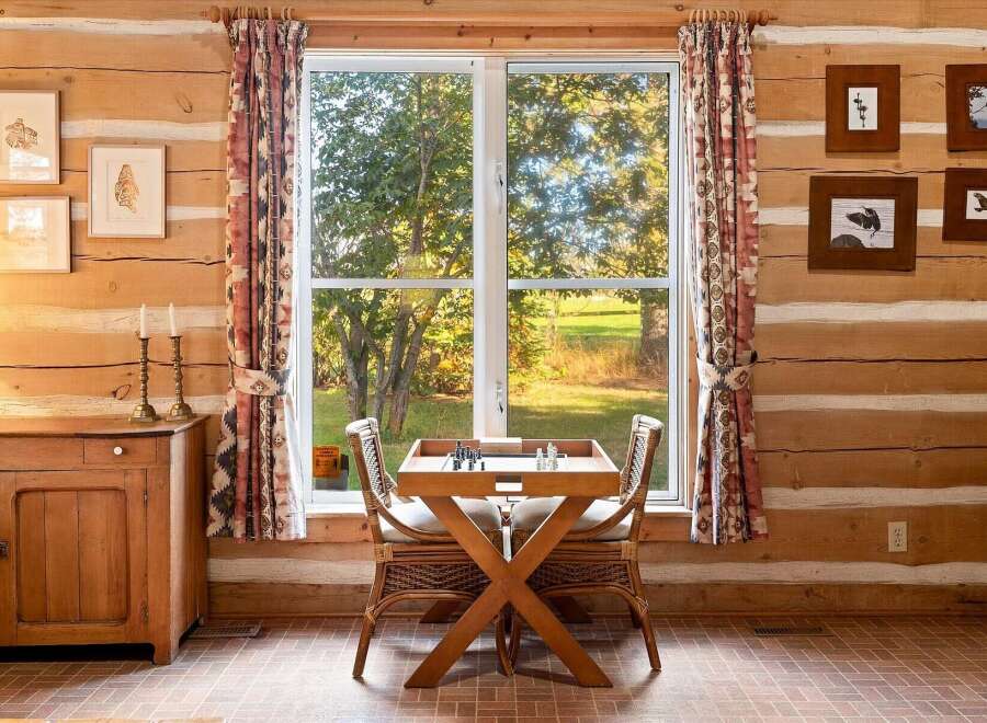 Experience rustic charm in this cozy log cabin featuring a dedicated chess table by the window, perfect for enjoying scenic views during a game.