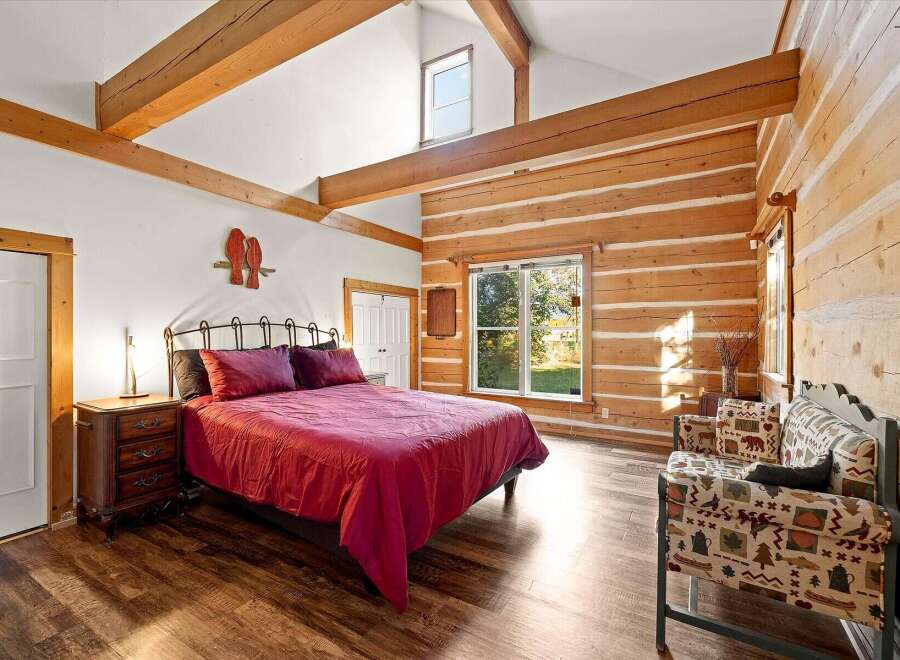 Experience rustic charm in this log cabin bedroom, featuring a vaulted ceiling with exposed wooden beams and a cozy king-size bed dressed in rich red linens.