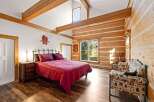 Experience rustic charm in this log cabin bedroom, featuring a vaulted ceiling with exposed wooden beams and a cozy king-size bed dressed in rich red linens.
