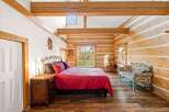 Experience rustic charm in this cozy log cabin bedroom, featuring a vibrant red comforter on a metal-frame bed and a charming patterned bench.