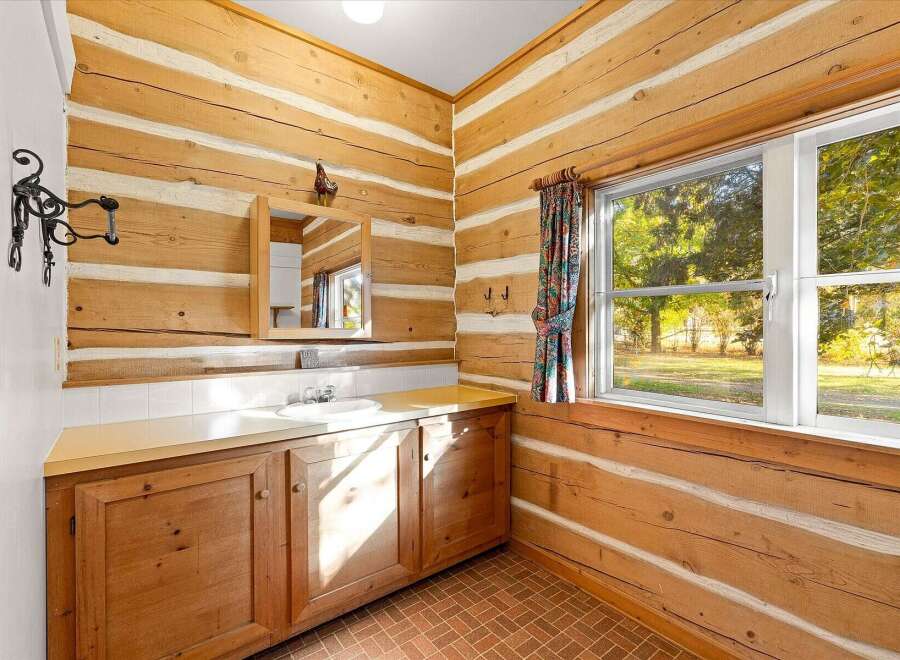 Experience rustic charm in this log cabin bathroom, featuring a functional vanity with ample storage and a bright, natural light-filled space.