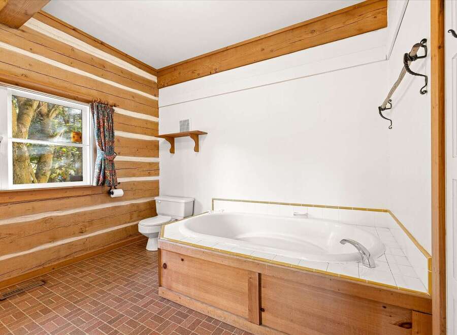 Experience rustic charm in this log cabin bathroom, featuring a spacious corner jetted tub with a warm wooden surround.