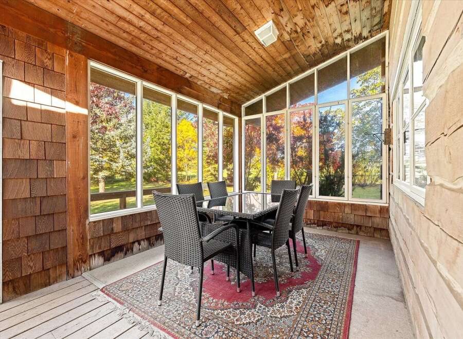 Enjoy breathtaking autumn views from this sunroom, featuring a glass-top dining table and six wicker chairs perfect for al fresco dining.