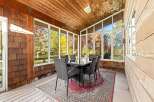 Enjoy breathtaking autumn views from this sunroom, featuring a glass-top dining table and six wicker chairs perfect for al fresco dining.