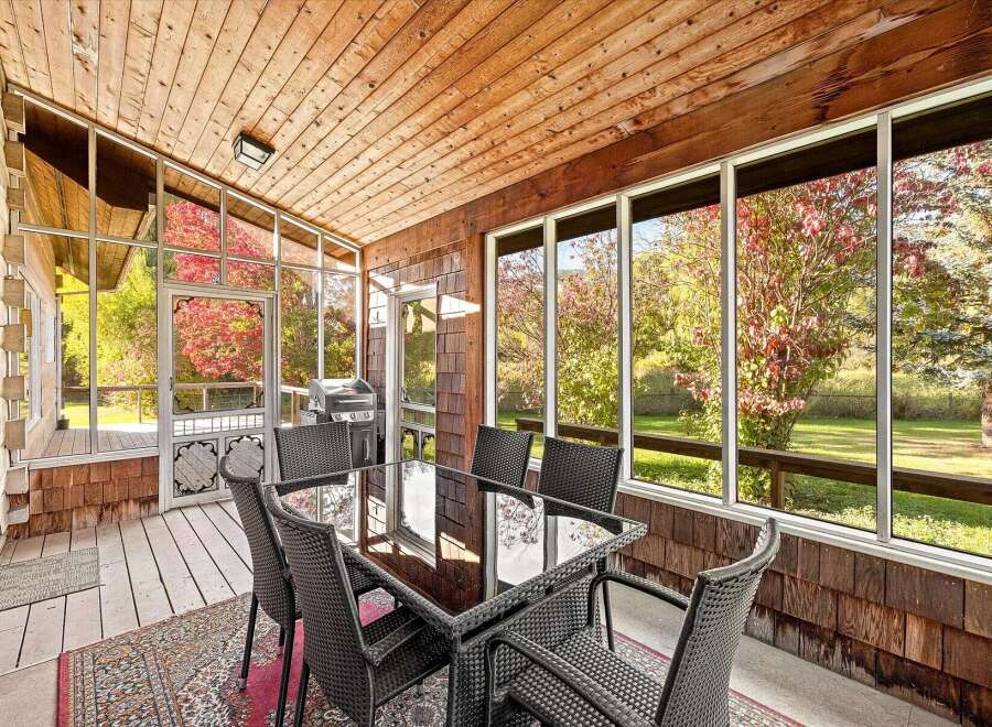 Enjoy the changing seasons from this enclosed sunroom, featuring a dining set perfect for al fresco meals.
