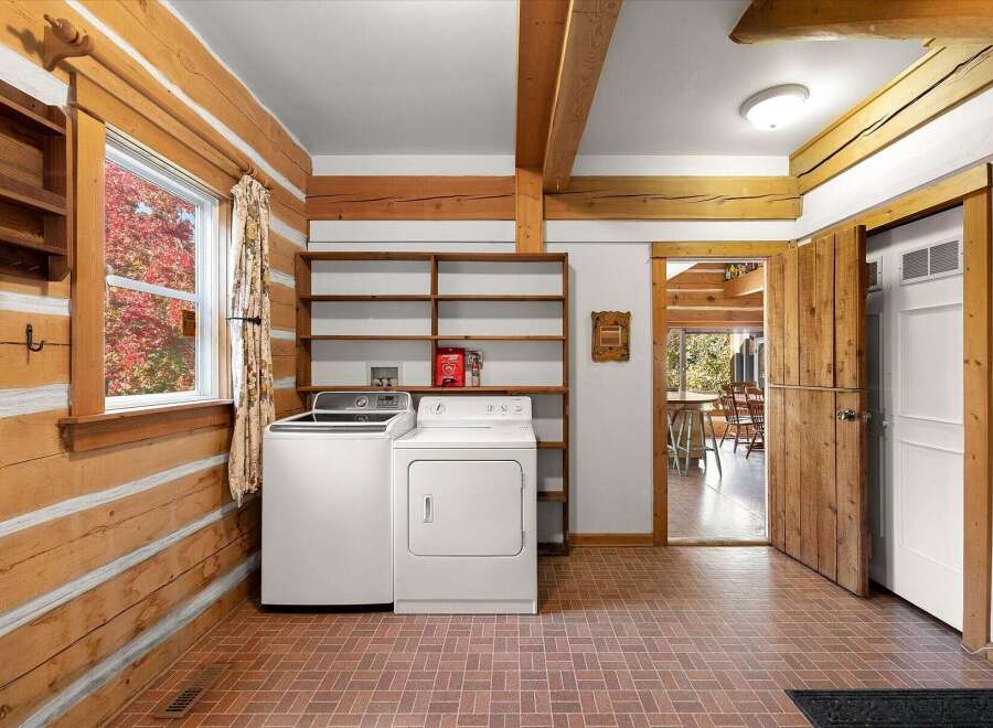 This charming log home laundry room features a white washer and dryer set against a backdrop of rustic log walls and exposed wooden beams.