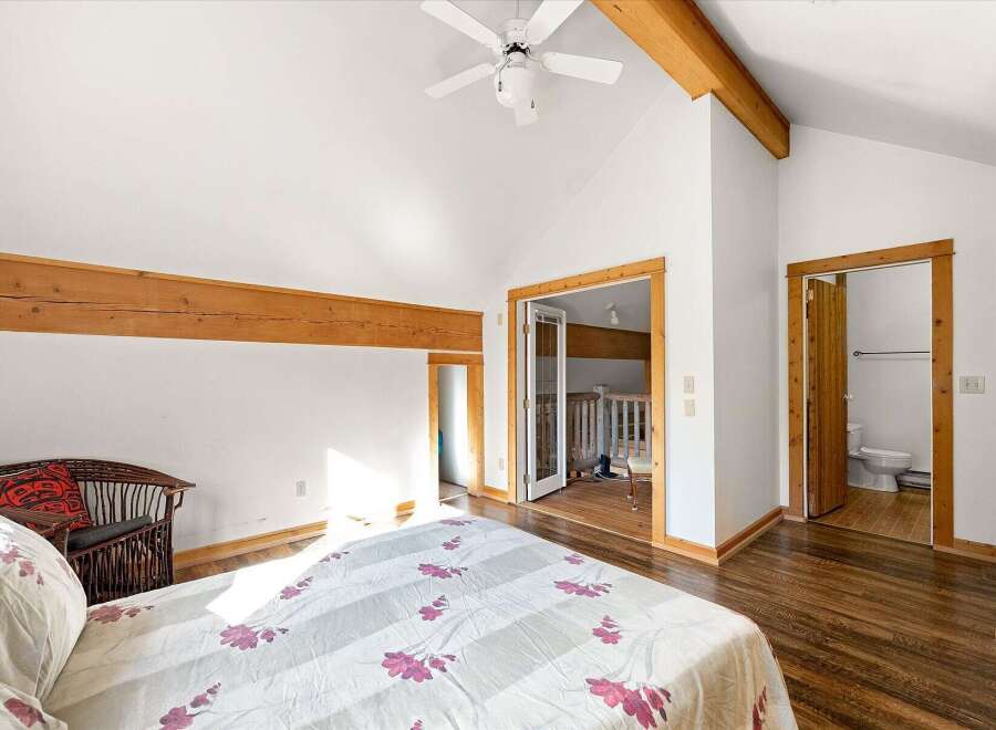 Experience rustic charm in this spacious bedroom featuring exposed wooden beams and a vaulted ceiling with a ceiling fan.
