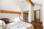 Experience rustic charm in this spacious bedroom featuring exposed wooden beams and a vaulted ceiling with a ceiling fan.