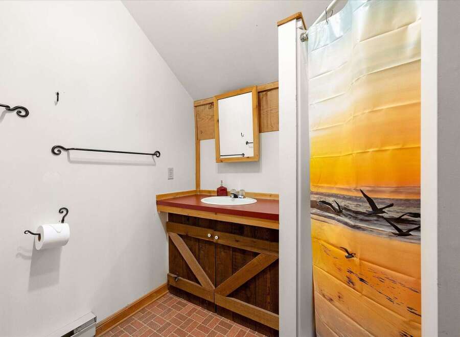 This charming bathroom features a rustic wooden vanity with a barn-style door design, complemented by a red countertop and a white sink.