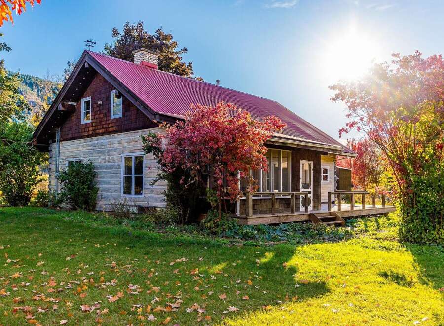 Embrace the charm of autumn with this picturesque home, featuring a vibrant red metal roof and rustic log siding.