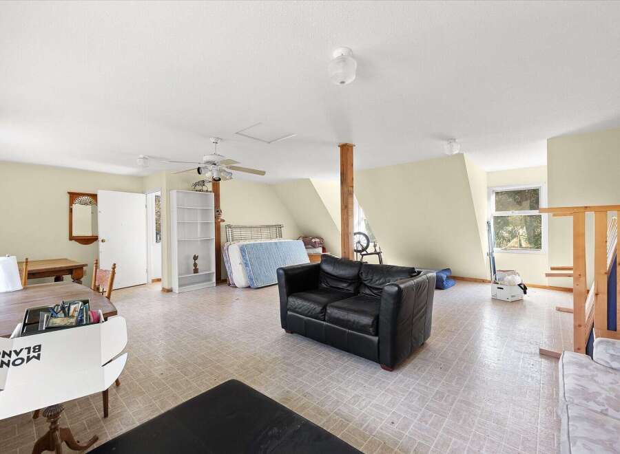 This spacious attic room offers versatile living potential with a comfortable black leather sofa and a dining area featuring a wooden table and chairs.
