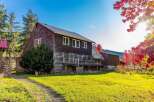 Experience the charm of autumn with this rustic property, featuring a weathered wooden barn and house set against a backdrop of vibrant red maple trees.