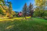Nestled amidst vibrant autumn foliage, this charming home boasts a picturesque setting with mature trees and a sprawling green lawn scattered with fallen leaves.