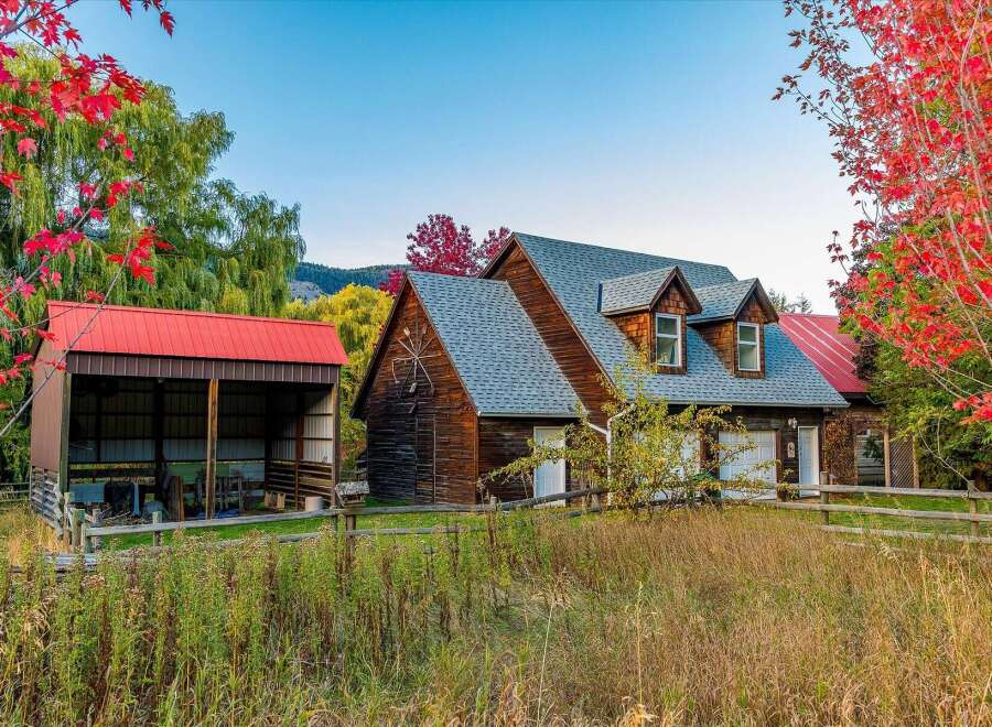 Experience rustic charm and autumn beauty at this picturesque property, featuring a classic wooden home with dormer windows and a detached red-roofed barn.