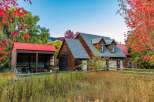 Experience rustic charm and autumn beauty at this picturesque property, featuring a classic wooden home with dormer windows and a detached red-roofed barn.