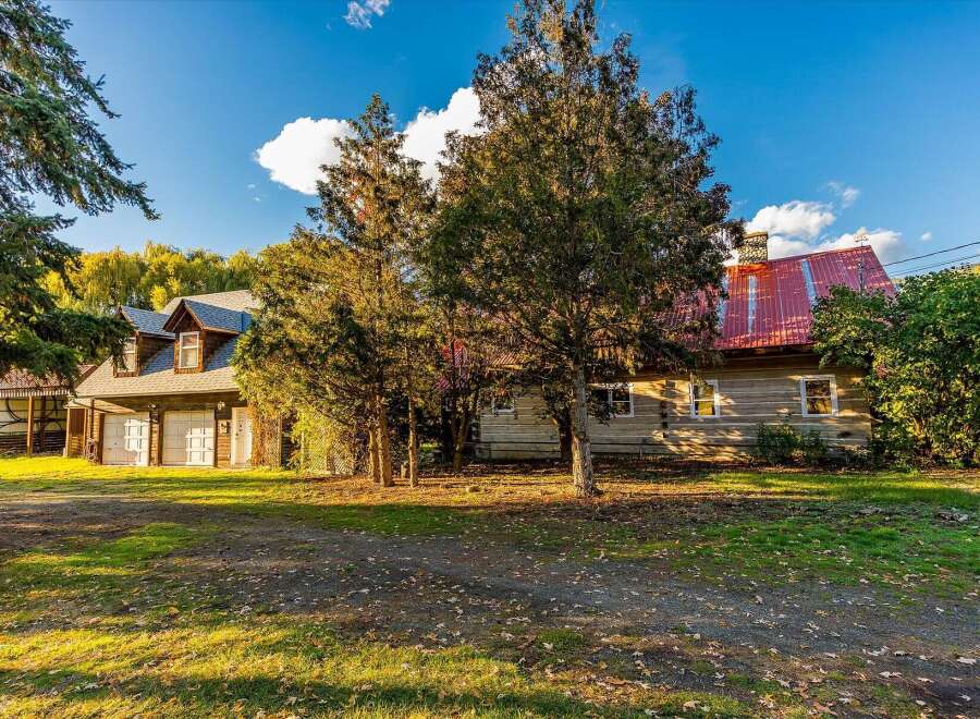 Nestled amidst mature trees, this charming log home offers a serene retreat with a bright red metal roof and a spacious attached garage.