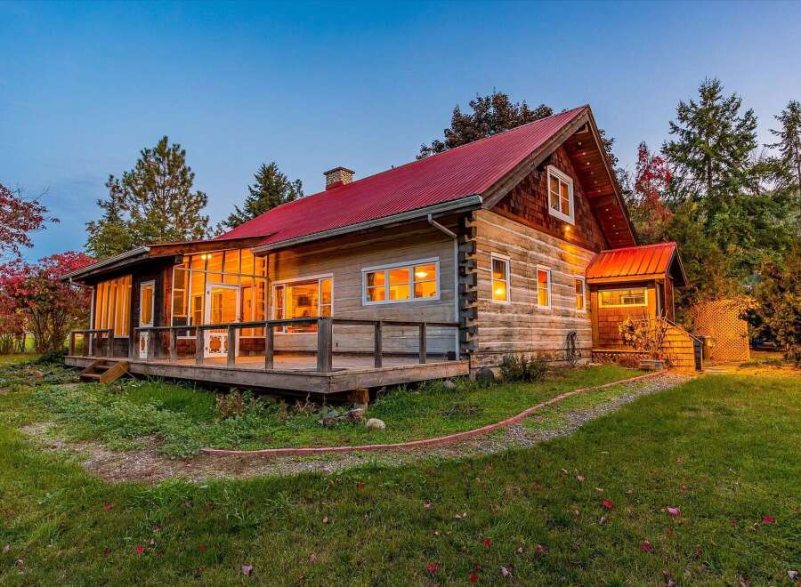 Experience rustic charm in this log cabin featuring a vibrant red metal roof and a spacious wrap-around deck perfect for enjoying the surrounding nature.