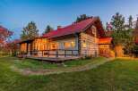Experience rustic charm in this log cabin featuring a vibrant red metal roof and a spacious wrap-around deck perfect for enjoying the surrounding nature.