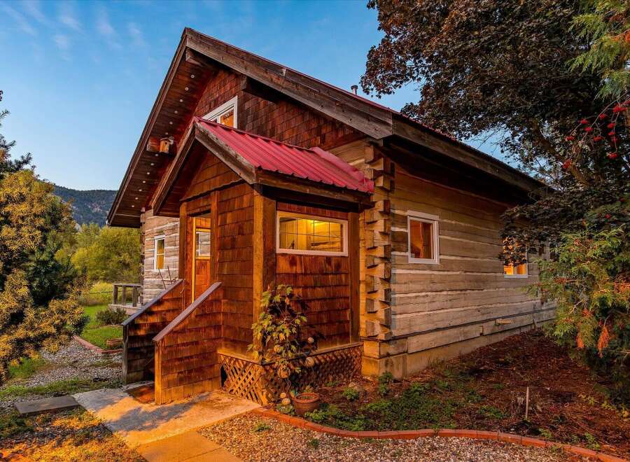 Experience rustic charm in this log cabin home, featuring a vibrant red metal roof and natural wood siding.
