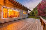 Enjoy the warm glow of this charming log home's interior, visible through its large windows, as dusk settles.