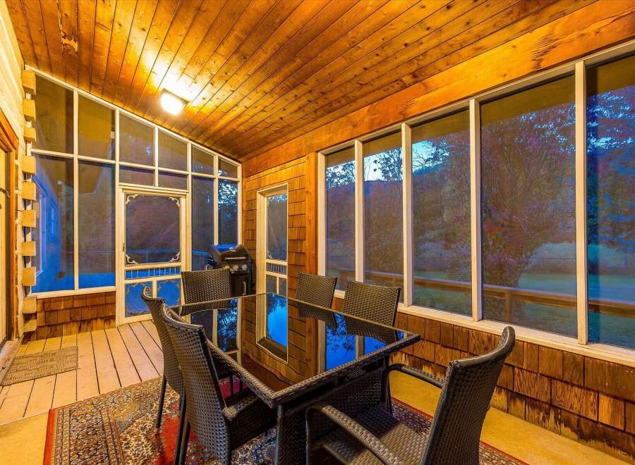 Enjoy outdoor dining and grilling on this charming screened-in porch, complete with a glass-top dining table and chairs.