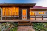 Step onto the inviting wooden porch of this charming home, featuring a rustic screened door and large windows that glow with warm interior light.