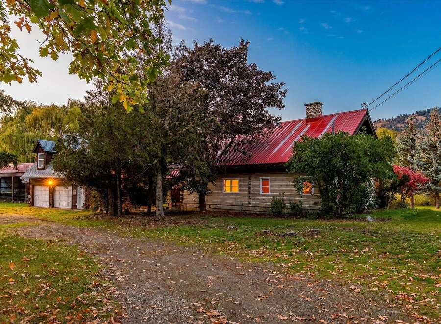 Experience rustic charm in this log cabin home, featuring a vibrant red metal roof and a cozy stone chimney.