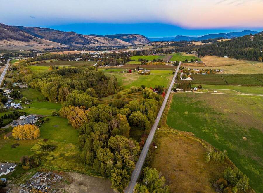 Experience the serene beauty of this rural landscape, featuring a picturesque road winding through lush green fields and vibrant autumn trees.